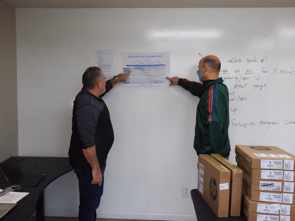 Two volunteers reading the build-day plan taped to a whiteboard, beside stacked computer cartons