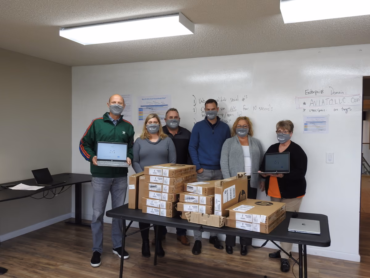 Volunteers and club staff standing behind a table stacked with boxed computers on a build day