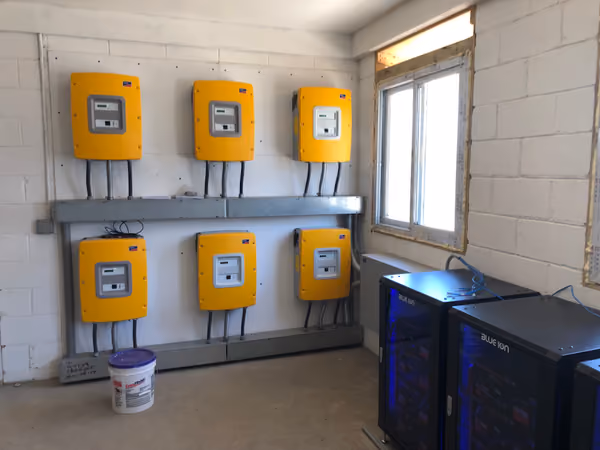 Six yellow solar inverters mounted on a wall above the battery cabinets they charge