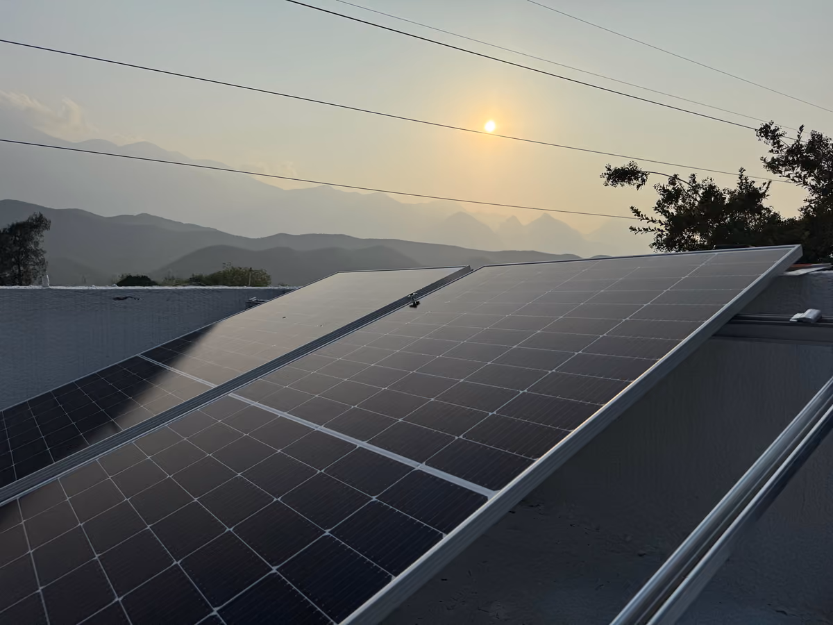 Rooftop solar panels newly installed at the Back2Back Ministries site in Monterrey, with the sun low over the mountains behind them