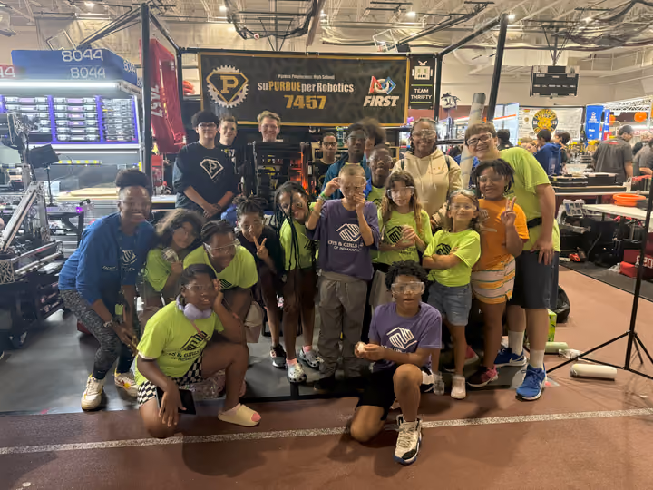 Club members and staff crowded around a FIRST Robotics team display at a competition