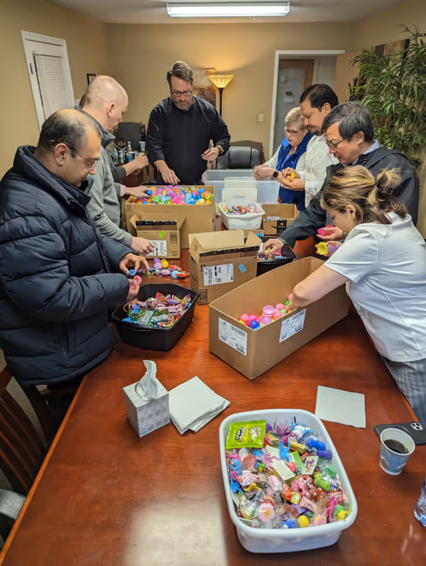 Volunteers standing around a boardroom table, filling bins with supplies for club members